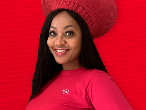 A portrait of Pelly Malebe on a red background. She is smiling, and wearing a red Roche shirt.